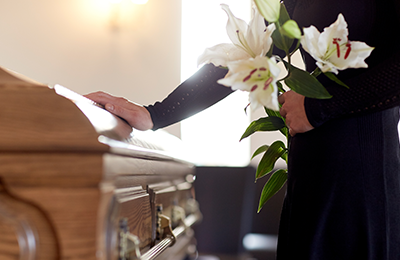 Woman holding flowers in hand and placing other hand on casket